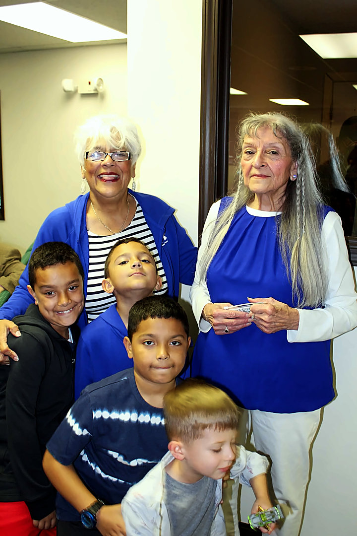 Two smiling women in blue tops stand together with four young boys gathered in front of them at a Freedom House Church event.